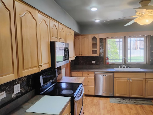 kitchen with appliances with stainless steel finishes, glass insert cabinets, decorative backsplash, a sink, and light brown cabinetry