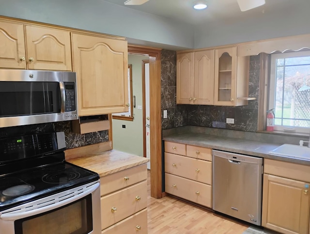 kitchen with glass insert cabinets, appliances with stainless steel finishes, light wood-style floors, light brown cabinetry, and backsplash
