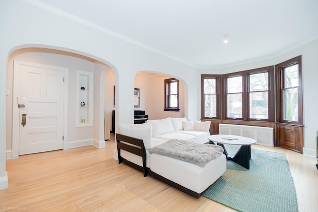 living area featuring radiator heating unit, arched walkways, light wood-style flooring, ornamental molding, and baseboards