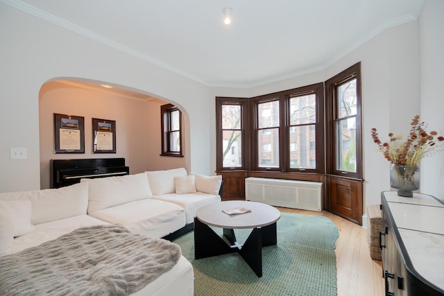 living area with radiator heating unit, light wood finished floors, ornamental molding, and arched walkways