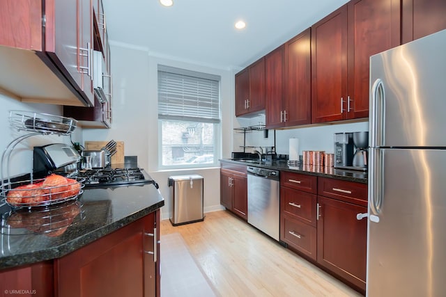 kitchen featuring stainless steel appliances, light wood finished floors, a sink, recessed lighting, and dark stone counters