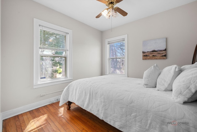 bedroom with wood finished floors, ceiling fan, baseboards, and multiple windows