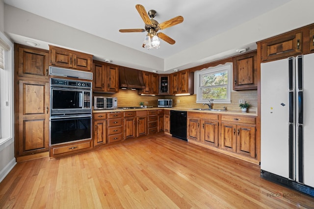 kitchen featuring light countertops, backsplash, exhaust hood, black appliances, and a sink
