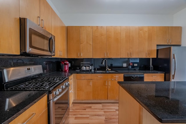 kitchen featuring dark stone countertops, a sink, appliances with stainless steel finishes, light wood-style floors, and backsplash