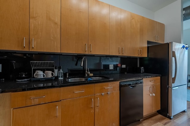 kitchen featuring dark stone countertops, a sink, dishwashing machine, backsplash, and light wood-style flooring
