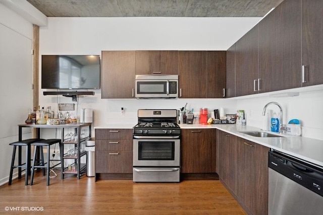 kitchen featuring stainless steel appliances, light countertops, a sink, light wood-type flooring, and dark brown cabinetry