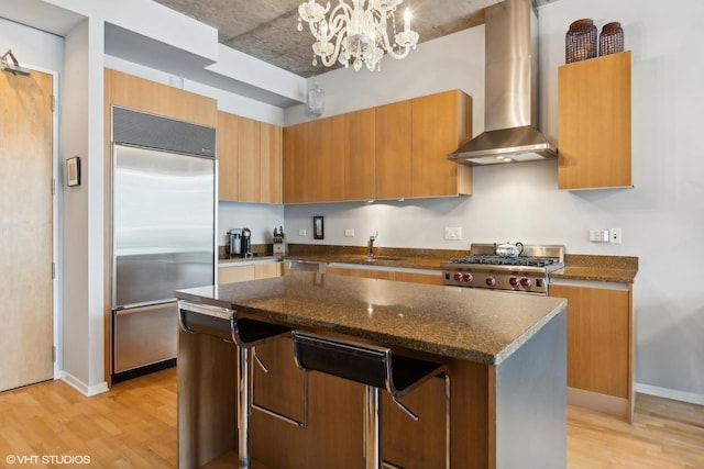 kitchen featuring wall chimney range hood, built in refrigerator, light wood-style floors, and dark stone countertops