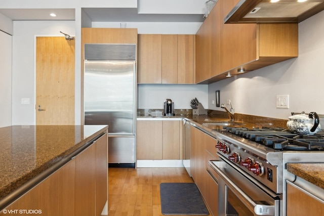 kitchen featuring dark stone countertops, high end appliances, light wood-type flooring, and under cabinet range hood