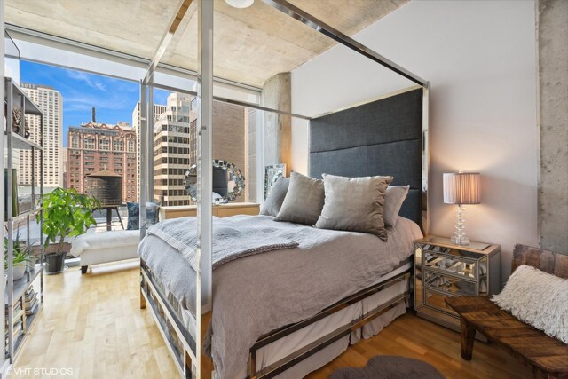 bedroom with wood finished floors, a view of city, and a wall of windows