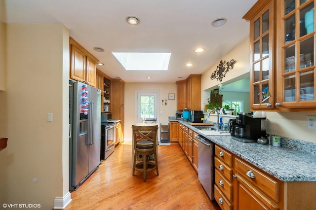 kitchen with appliances with stainless steel finishes, light wood-type flooring, brown cabinetry, a skylight, and a sink