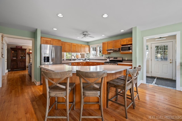 kitchen with a sink, appliances with stainless steel finishes, light countertops, under cabinet range hood, and recessed lighting