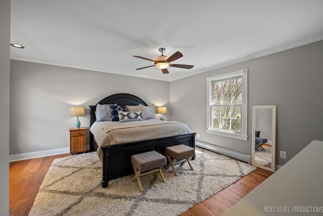 bedroom with a baseboard heating unit, wood finished floors, and ornamental molding