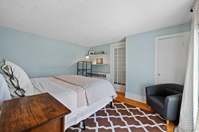 bedroom with radiator, wood finished floors, and baseboards