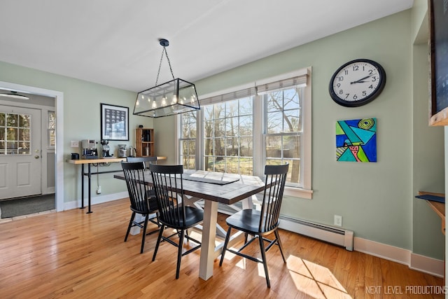 dining area with a baseboard heating unit, a notable chandelier, baseboards, and light wood-style floors