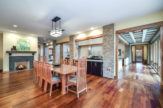 dining space with a tiled fireplace, wood finished floors, recessed lighting, and beam ceiling