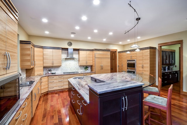kitchen with wall chimney range hood, a sink, dark wood-style flooring, a kitchen island with sink, and decorative backsplash