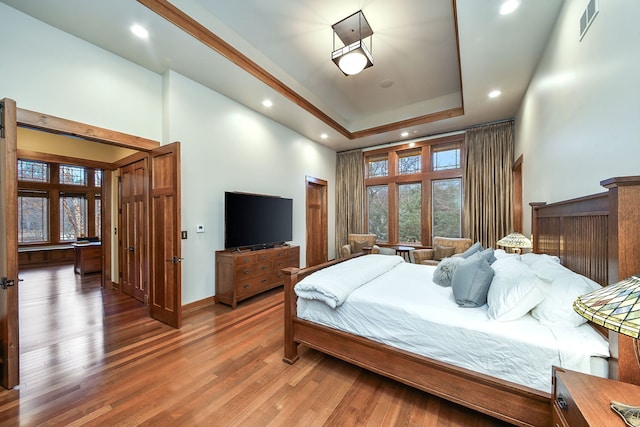 bedroom featuring recessed lighting, a tray ceiling, wood finished floors, a high ceiling, and baseboards