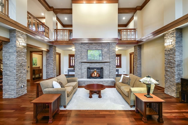 living area featuring a high ceiling, decorative columns, a fireplace, crown molding, and wood finished floors