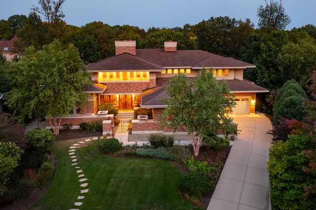 prairie-style house featuring driveway, a front lawn, an attached garage, and a chimney