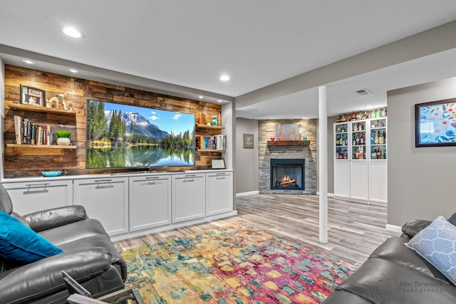 living room featuring a stone fireplace, recessed lighting, wood walls, visible vents, and light wood finished floors