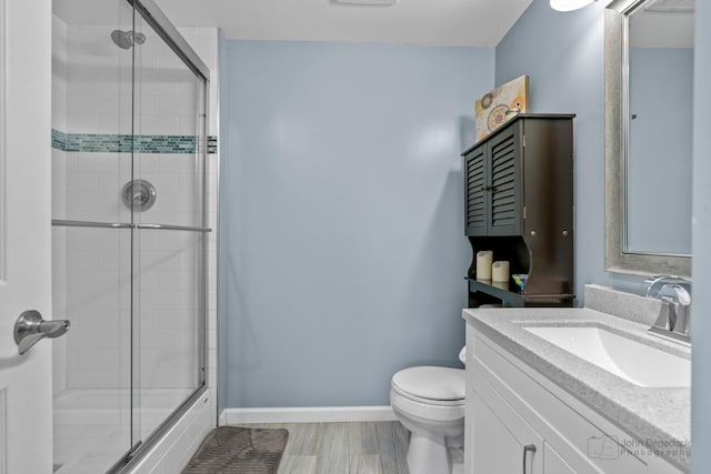 bathroom featuring a shower with shower door, vanity, baseboards, and toilet
