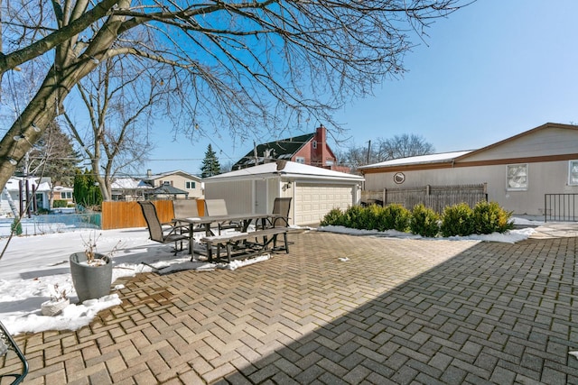 snow covered patio with outdoor dining space, an outdoor structure, fence, and a garage