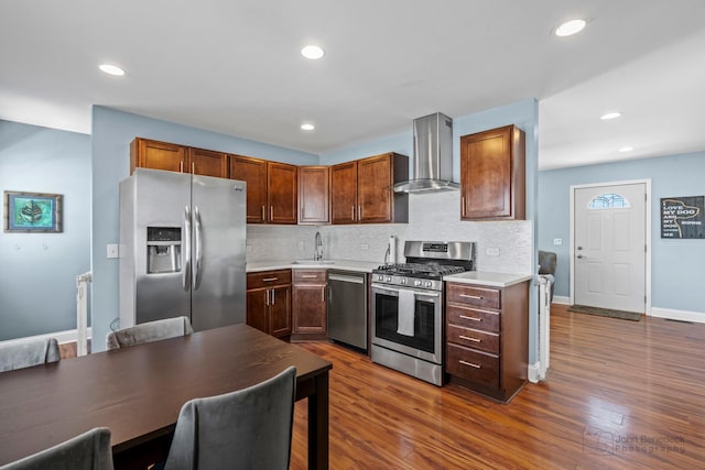 kitchen featuring wall chimney exhaust hood, light countertops, appliances with stainless steel finishes, dark wood finished floors, and decorative backsplash