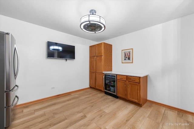 kitchen with beverage cooler, freestanding refrigerator, brown cabinetry, and light wood-style floors