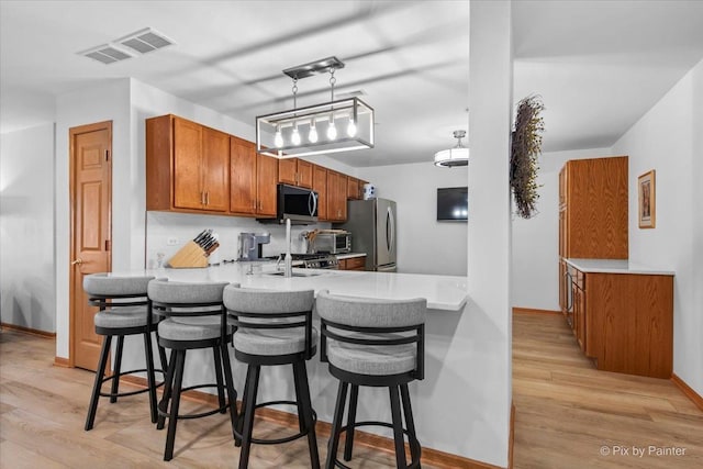 kitchen featuring visible vents, appliances with stainless steel finishes, brown cabinets, and a kitchen bar