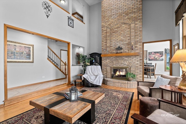 living room with a high ceiling, wood finished floors, stairs, a fireplace, and baseboards