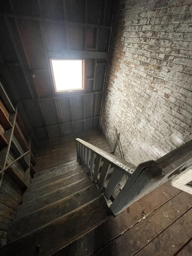 stairs with hardwood / wood-style floors and brick wall