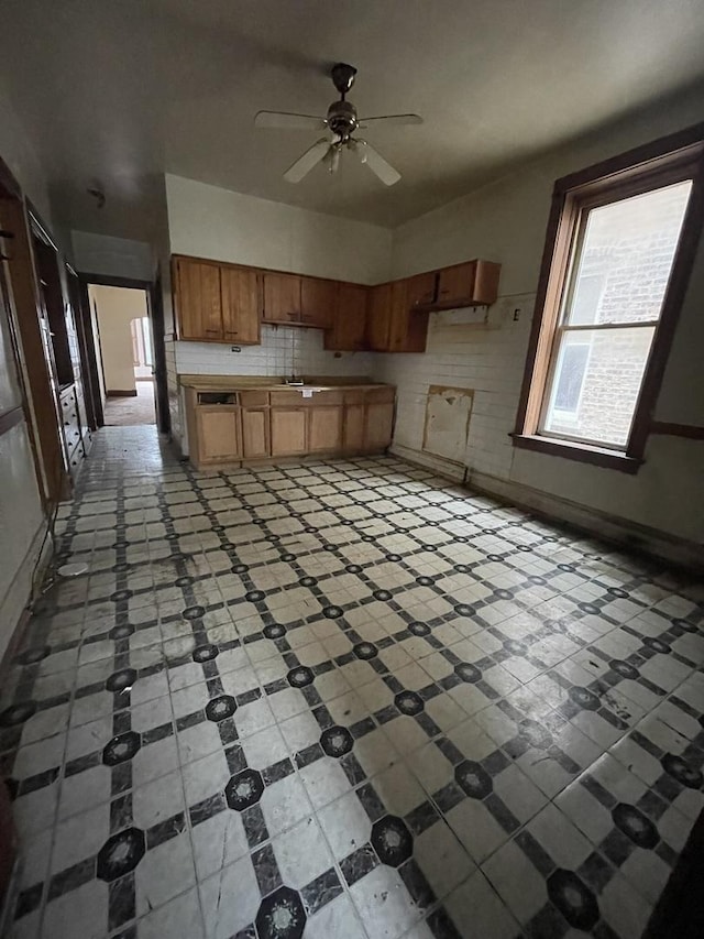 kitchen featuring tasteful backsplash, baseboards, light countertops, brown cabinetry, and ceiling fan