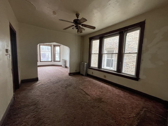 spare room with radiator heating unit, arched walkways, and plenty of natural light