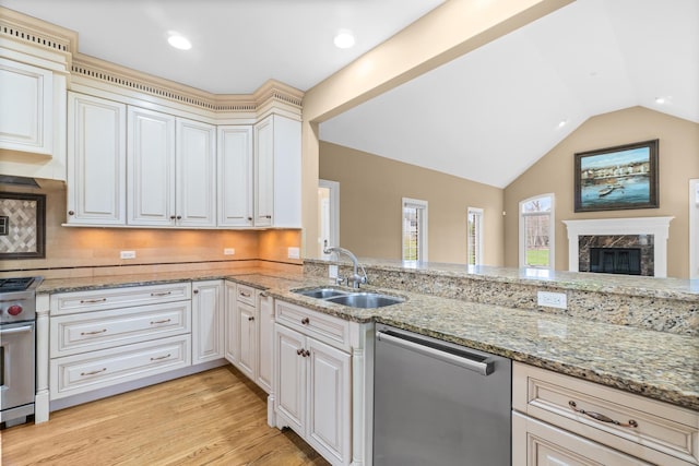 kitchen featuring stainless steel appliances, a sink, light wood-style floors, light stone countertops, and lofted ceiling