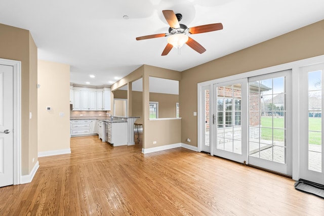 unfurnished living room featuring light wood-style flooring, a sink, baseboards, and a ceiling fan