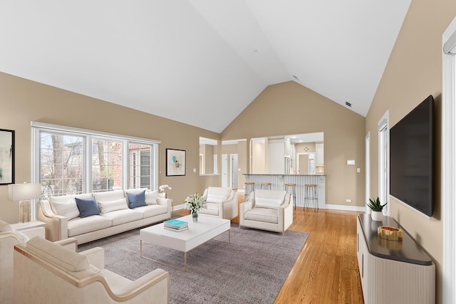 living room with high vaulted ceiling, light wood-style flooring, and baseboards