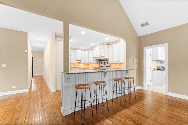 kitchen featuring a kitchen breakfast bar, a peninsula, white cabinetry, visible vents, and dark stone counters