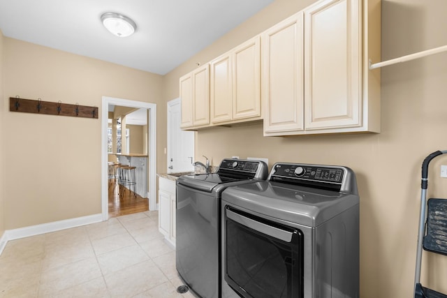 laundry area with baseboards, light tile patterned floors, washing machine and clothes dryer, cabinet space, and a sink