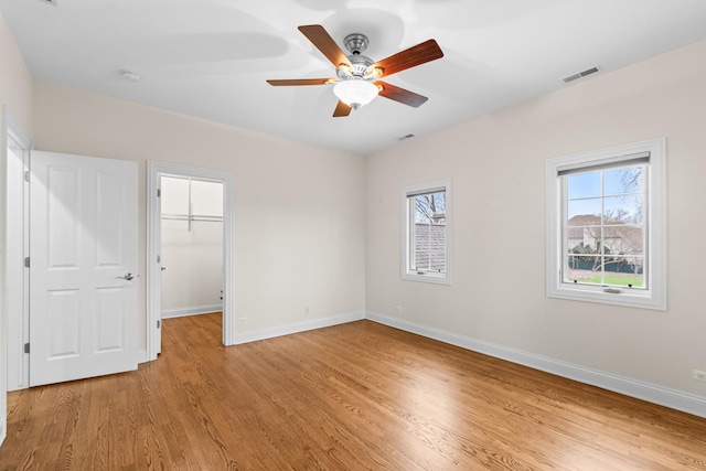 unfurnished bedroom featuring light wood-style floors, visible vents, baseboards, and a walk in closet