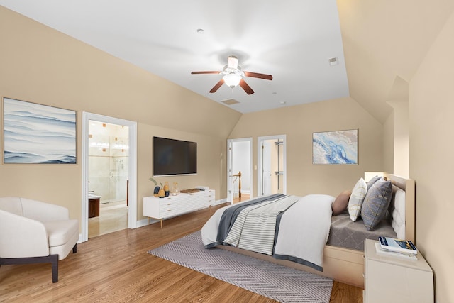 bedroom featuring visible vents, light wood finished floors, ensuite bathroom, and vaulted ceiling