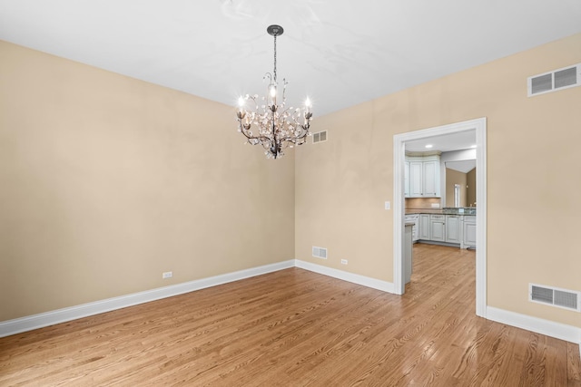 unfurnished room featuring light wood-style floors, a notable chandelier, and visible vents
