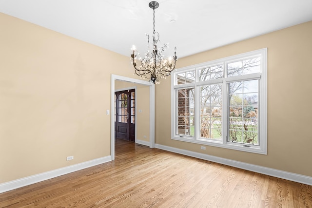 unfurnished dining area with a chandelier, light wood-style floors, and baseboards