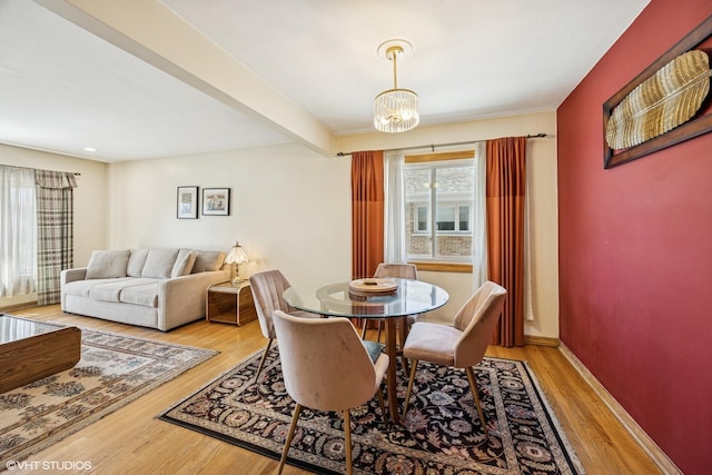 dining space with beamed ceiling, baseboards, a notable chandelier, and wood finished floors