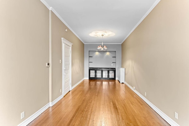 unfurnished dining area with crown molding, an inviting chandelier, baseboards, and light wood-style floors