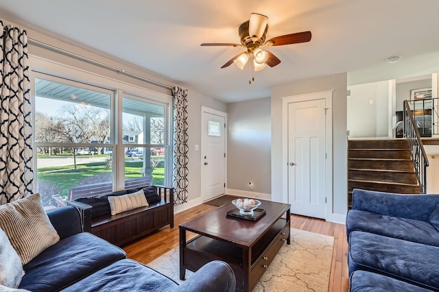 living area with light wood-style flooring, baseboards, a ceiling fan, and stairway