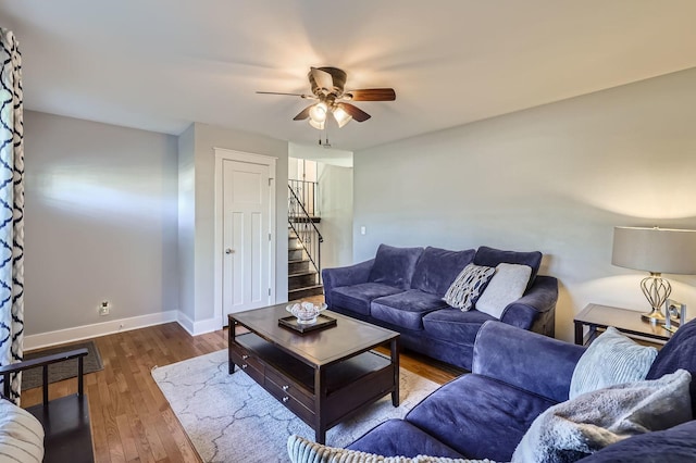 living area with wood finished floors, ceiling fan, baseboards, and stairway