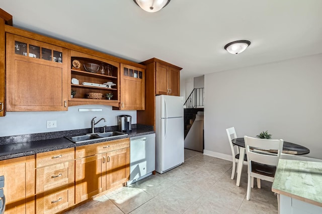 kitchen featuring glass insert cabinets, freestanding refrigerator, brown cabinetry, stainless steel dishwasher, and a sink