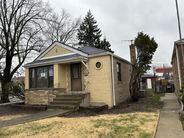 bungalow-style home featuring brick siding, central air condition unit, and a chimney
