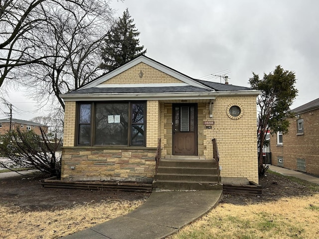 bungalow featuring roof with shingles, brick siding, and stone siding