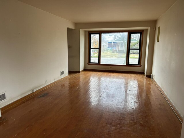 unfurnished room with wood finished floors, baseboards, and visible vents